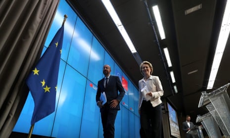Michel and von der Leyen  walk off stage clutching papers smiling past EU flag.
