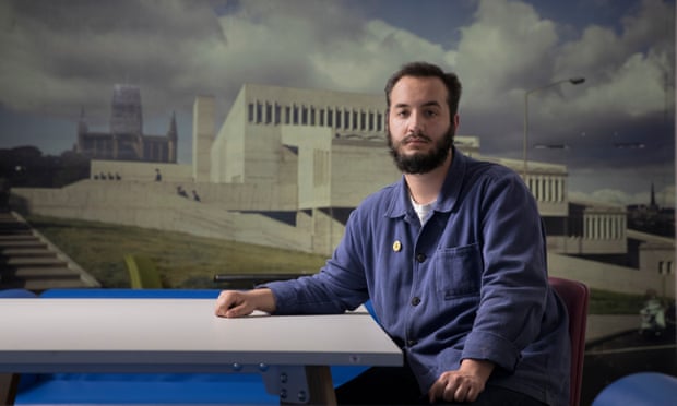 Josh Freestone sitting at a desk in front of large image of a modern building