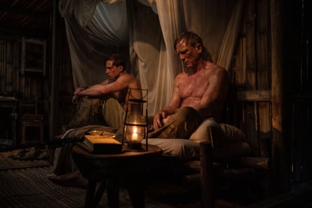 Two topless men sit on wooden bed