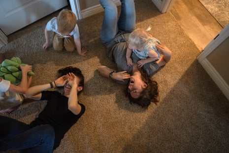 Two women and three young kids play on the carpeted ground indoors
