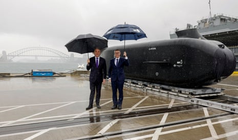The men shelter under umbrellas in front of a small black submarine
