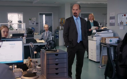 he is a tall, middle-aged man with a goatee beard and mostly bald head, wearing a suit and tie, standing in an office.