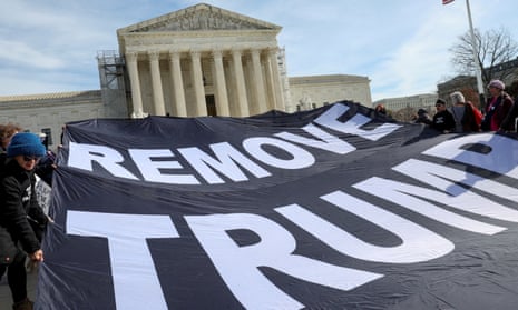 A group of people dressed in cold-weather gear hold a black cloth banner with white letters that spell Remove Trump, which is perhaps 10 feet by 20 feet, with a judicial building in the background.