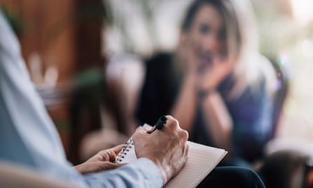 therapist writing down notes as a woman sits in the background