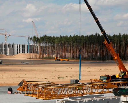 Construction equipment on a deforested area of land and in the background some remaining trees and cranes the shell of the factory