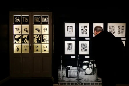 black and white drawings, including a large one of a drum kit, are mounted on a black wall. The man is dressed in black and has his back to the camera; the drawings, on white or pale paper, are illuminated and stand out from the background.