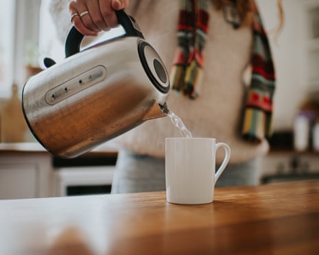 A woman pours boiling water from a modern chrome kettle into a white mug