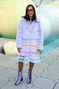 Zeena is wearing a light purple fake fur jacket with a dress of many pastel shades and purple and black two-tone ankle boots.
