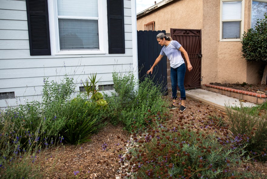 woman gestures downward next to house