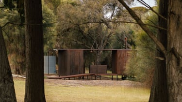 The Ablutions at Wybalenna, a rusted metal cabin on stilts, stands among trees