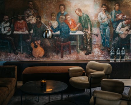 A lounge area with 70s leather chairs and a mural of people playing instruments and talking and drinking on the wall
