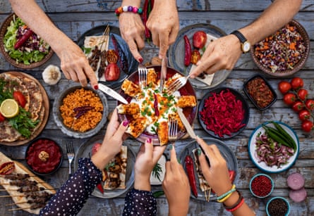 A selection of shared plates taken from above with four people’s hands reaching to take the same food from one plate
