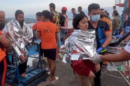 People wrapped in foil blankets are led off a vessel