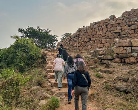 A group of women walk up a path beside a stone wall in Delhi