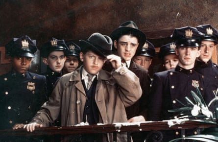 Boy at front dressed like a detective with a fawn mac and wearing a black hat while behind him is a crowd of US police officers