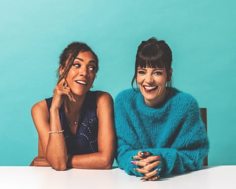 Lily Allen and Miquita Oliver sit at a desk together smiling against a turquoise background, they were photographed in London for the Observer New Review in June 2024.