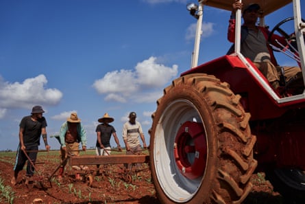Four people hold a plough being pulled by a tractor