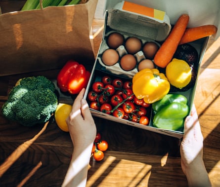 A woman opens a home delivery cardboard box filled with multicoloured fresh organic fruits, vegetables and groceries