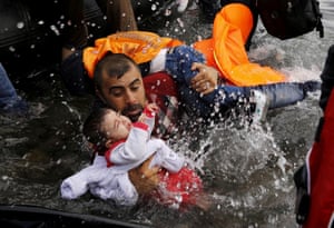 A Syrian refugee holds onto his children as he struggles to walk off a dinghy on the Greek island of Lesbos, after crossing a part of the Aegean Sea from Turkey to Lesbos 24 September, 2015