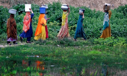 Women in colourful dress carry pots of water on their heads.