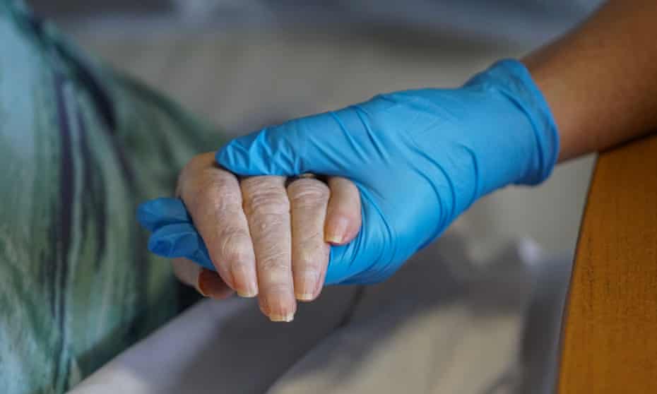 Hand with blue latex glove holds older woman’s hand