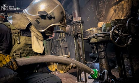 A rescuer wearing a shiny metal helmet holds a hose at the site of a Russian strike. 