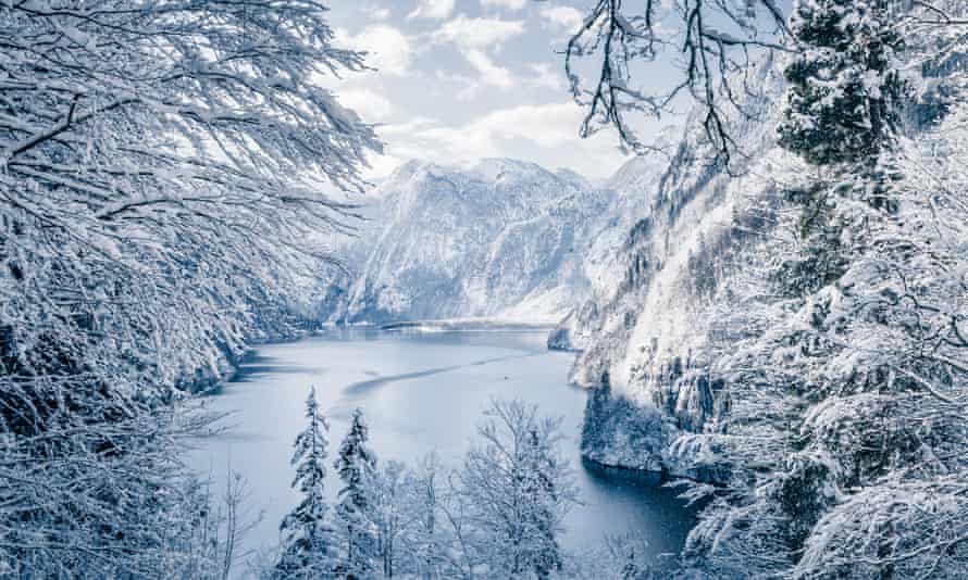 Un lac gelé entouré d'arbres enneigés et de montagnes derrière