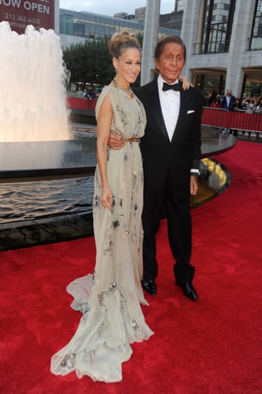 Valentino stands with his arm around Sarah Jessica Parker on a red carpet and in front of a fountain