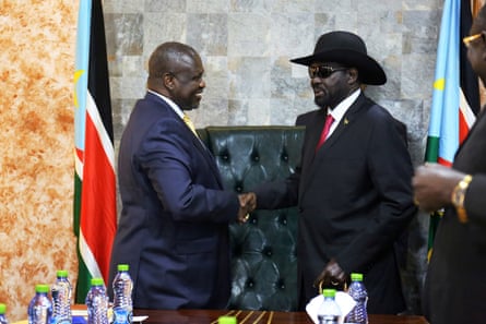 Two men shaking hands in a government building next to the flag of South Sudan