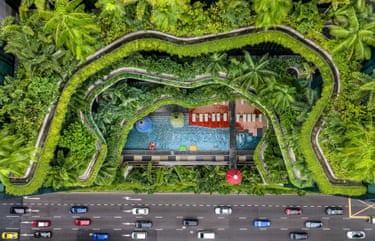 Aerial view of a hotel rooftop pool and cabanas framed by lush tiered gardens above a busy Singapore road