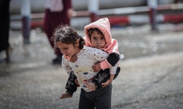 A Palestinian child carries her sister on her back as they flee Rafah