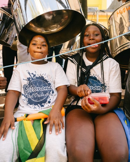 Two young people in Metronome Steel Orchestra T-shirts, with a steel drum behind them