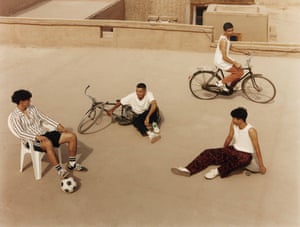 Four young people, two with bicycles, one with a football and one with a skateboard