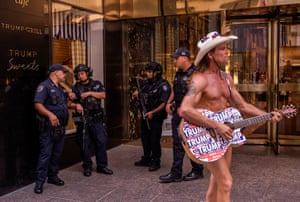 The Naked Cowboy, apparently wearing only a Stetson and holding a guitar covered in Trump stickers across the middle of his body, performs outside Trump Tower