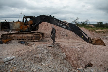 A member of Brazilian security forces walks next to a charred excavator in a dug-up area