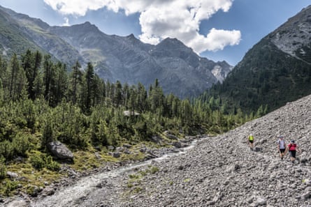 Walkers on a path through scree in a wooded valley between mountains