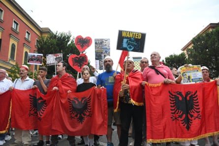 Protesters stand with red flags bearing a black double-headed eagle. Placards include one that reads 'Wanted' beside a picture of Edi Rama