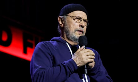 a man wearing a sweatshirt and beanie stands on stage with a microphone