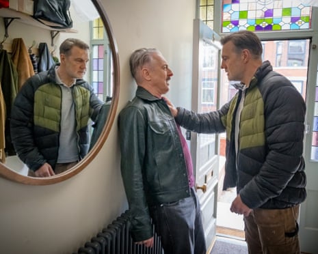 David Morrissey and Alan Cumming stand face to face at an open doorway with colorful stained glass above