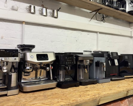 Lineup of eight different bean-to-cup coffee machines on a wooden countertop.