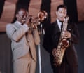 Two men in suits on stage, one playing trumpet, one saxaphone