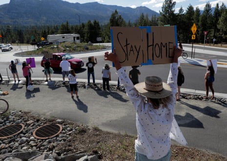 A woman standing with a group of people near a traffic roundabout holds a sign over her head that reads ‘Stay home’.