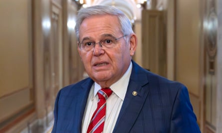 Older white man with white hair, classes, navy suit and red tie standing in hallway.