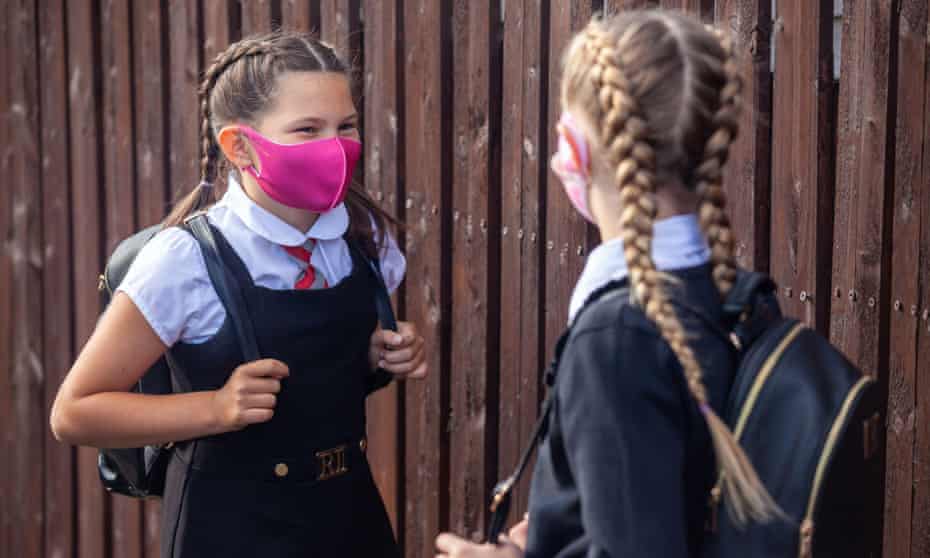Two 10 year old school friends chatting to each other and wearing face masks