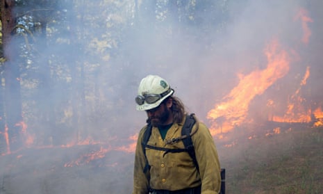 Firefighter standing in foreground with wildfire burning behind him