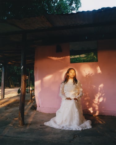 Novia llanera, 2022 . A young woman in a bridal gown sits outside a house in the evening light