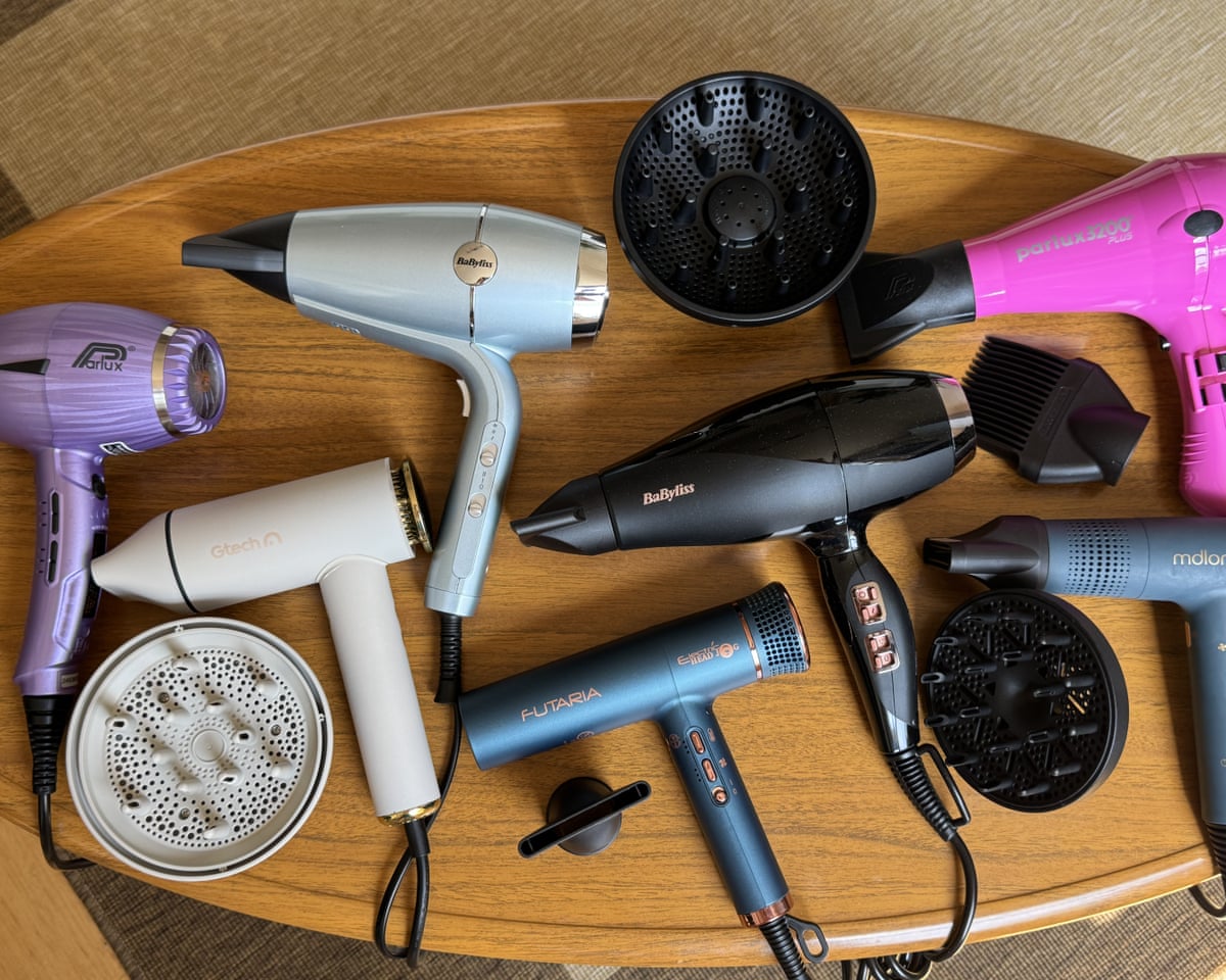 Seven different hairdryers photographed from above on a wooden coffee table.