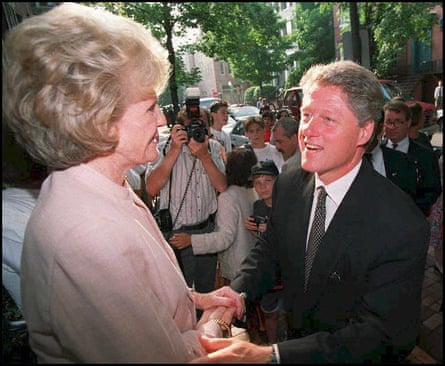 Bill Clinton greets Pamela Harriman. A crowd of people, with one taking a photograph, can be seen in the background.