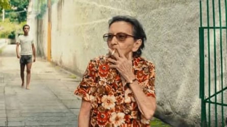 Tânia Maria smokes a cigarette while wearing a brightly patterned flora shirt.