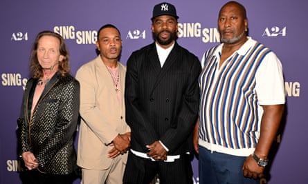 four men stand in front of wall with 'sing sing' on it